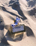 ZOLYQUE The Hair Perfume bottle resting on sandy beach, showcasing its elegant design and luxurious scent.