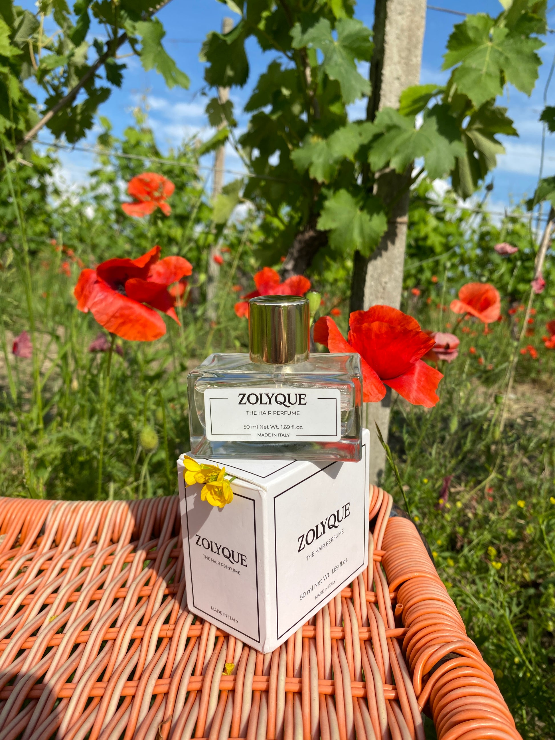 Hair perfume bottle by Zolyque surrounded by vibrant flowers in a sunny outdoor setting, showcasing Italian elegance.